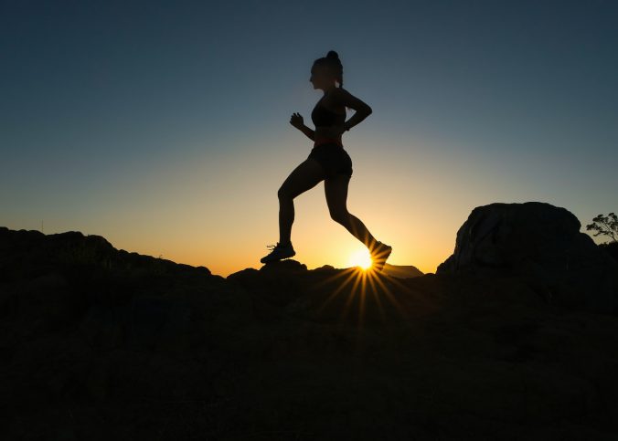 silhouette of man jumping on rocky mountain during sunset